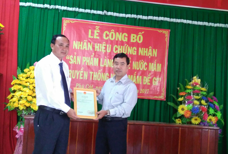 Ông Nguyễn Hữu Hà, Phó Giám đốc Sở Khoa học và Công nghệ tỉnh Bình Định (trái) trao giấy chứng nhận nhãn hiệu nước mắm truyền thống Đề Gi cho UBND huyện Phù Cát.