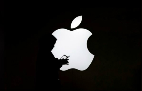  Một phụ nữ nhìn vào màn hình điện thoại di động của mình trước logo bên ngoài Apple Store ở Thượng Hải, Trung Quốc. Ảnh: Reuters