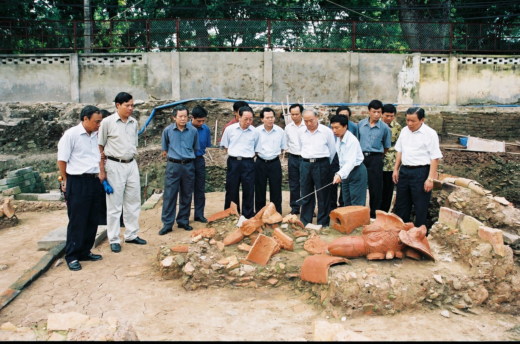 Đầu chim phượng và lá đề bằng đất nung nằm tại vị trí được khai quật. Chủ nhiệm dự án Tống Trung Tín và Chủ tịch Viện Khoa học và Xã hội Việt Nam Đỗ Hoài Nam (thứ ba từ trái qua) đang giới thiệu những mảnh võ của mái cung điện thời Lý với các vị lãnh đạo (khu A). Ảnh: Viện Khảo cổ học (2004).