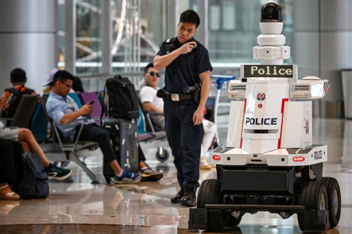 Nhân viên lực lượng cảnh sát Singapore đi tuần cùng một robot cảnh sát tại sân bay Changi ở Singapore. Ảnh: AFP