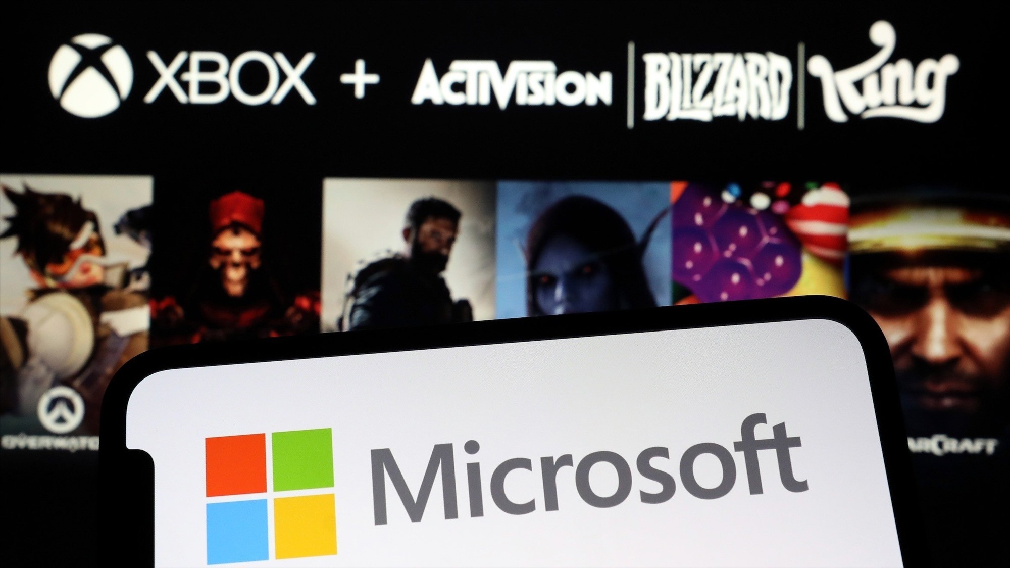 Logo Microsoft trên smartphone, phía sau là logo và hình ảnh trò chơi của Activision Blizzard. Ảnh: Reuters 